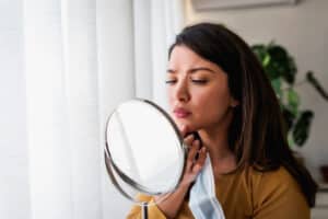 Woman looking in the mirror at her acne needing treatment in Evergreen, CO