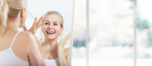 Beautiful blonde woman smiles at her reflection, happy with the effects of her Botox even months later