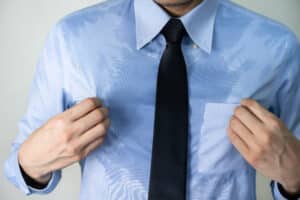Man wearing business clothing pulls his drenched shirt away from his body before his Botox® treatment for excessive sweating